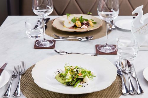 Fine dining table setting with textured place mats and two plates of carefully prepared food, polished cutlery and wine glasses