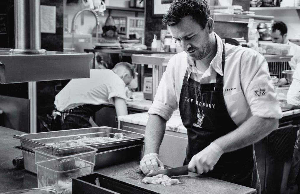 Candid black and white photo of chef Greg Austin prepping  in the kitchen of The Ledbury, London