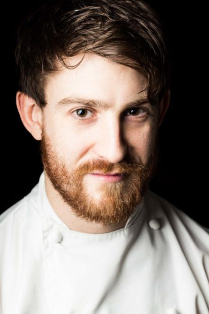 Head shot of chef Lee Westcott for Art Culinaire magazine. Chef is wearing chef whites, has a beard and the background is very dark