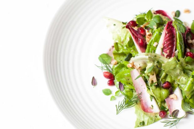 A salad with crisp lettuce, endive, herbs and pomegranate seeds, on a white plate