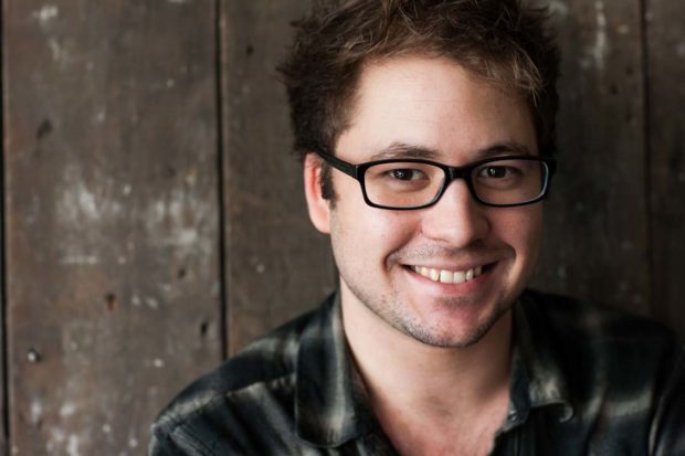 Natural light portrait of Dan Joines smiling. Young male, brown hair, wearing dark framed glasses