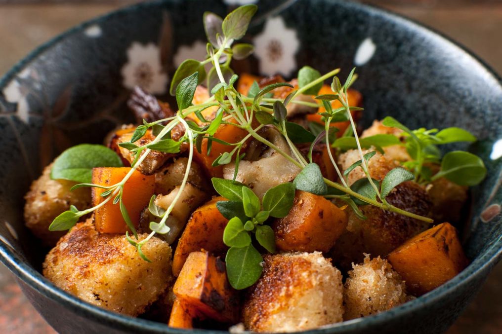 A dark and flower pattern bowl containing cooked gnocchi with roasted sweet potato garnished with fresh herbs