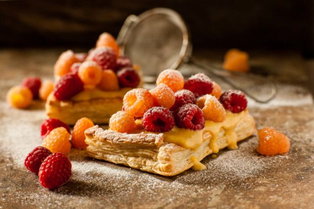 Puff pastry square topped with vanilla custard, with red and golden raspberries, dusted with icing sugar