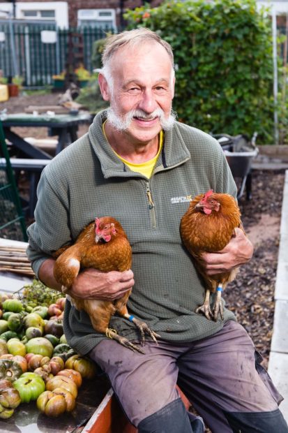 Organic gardener with handlebar mustoch in his allotment holding two chickens, one in each hand, for Liverpool Football Club