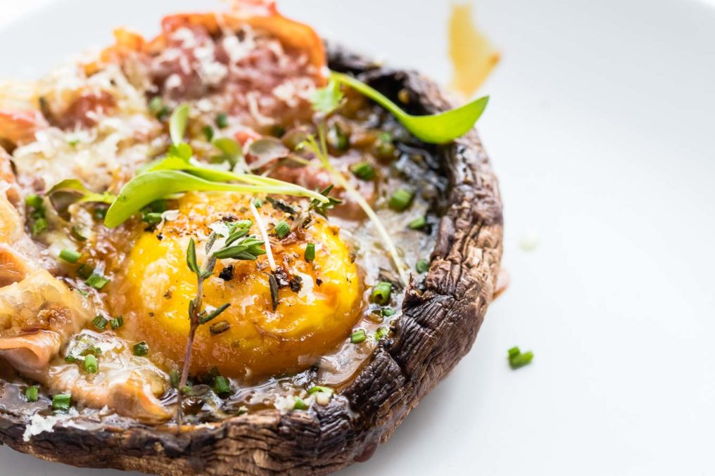 Close up photo of a baked portobello mushroom with a baked egg and pancetta with green micro herbs