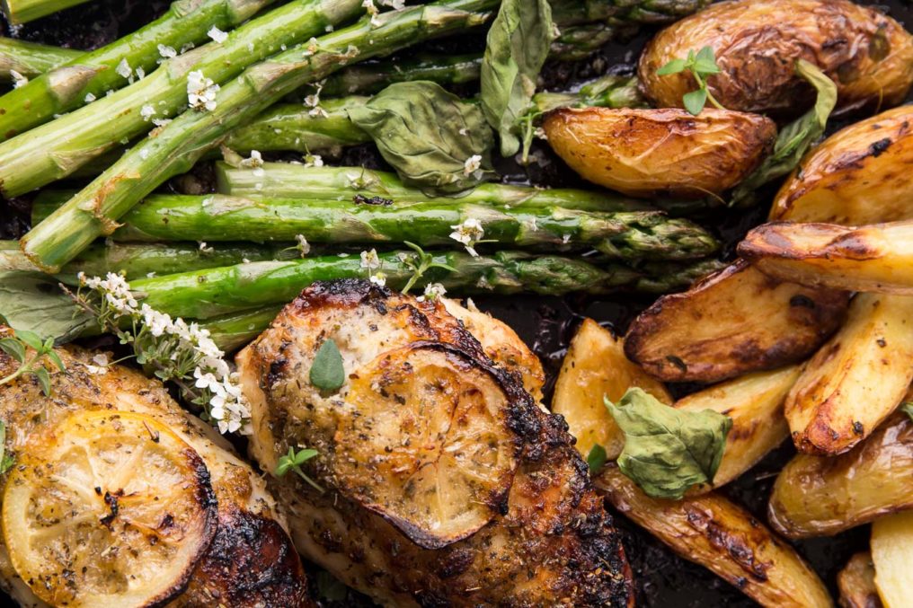 Top down photo of roasted lemon chicken breast with asparagus and roast potatoes garnished with small white wild flowers