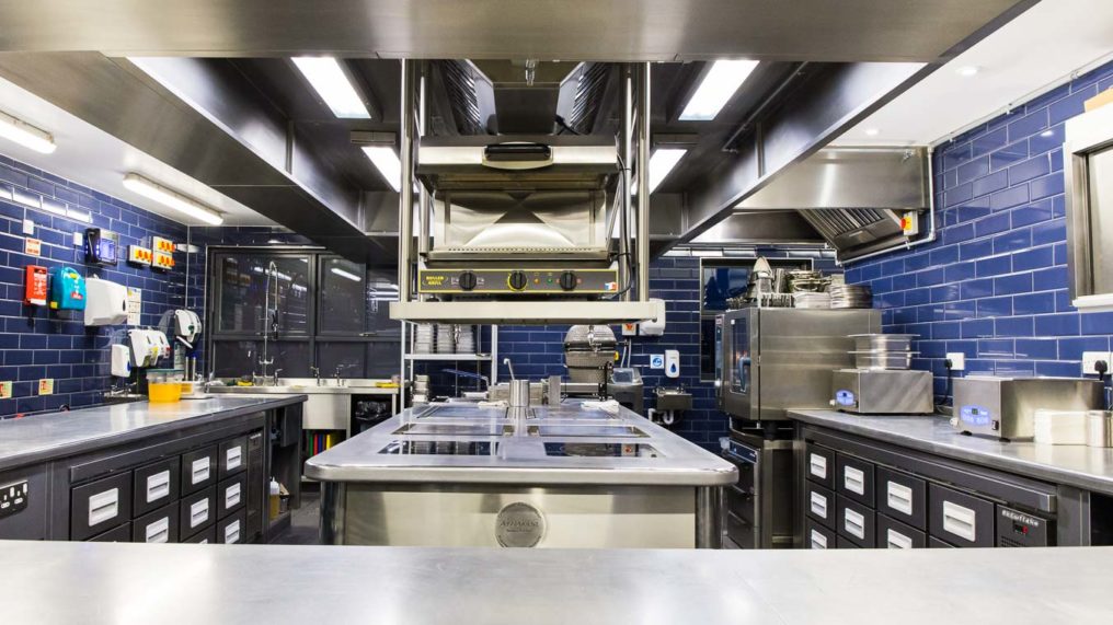 Pristinely clean commercial kitchen with stainless steel surfaces and blue tiles. Kitchen of The Oxford Blue gastropub
