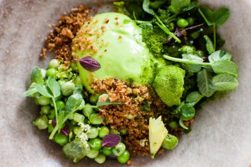 A stone dish with a round greenmail of pea mousse, with a crumb, peas, pea chutes and small mint leaves
