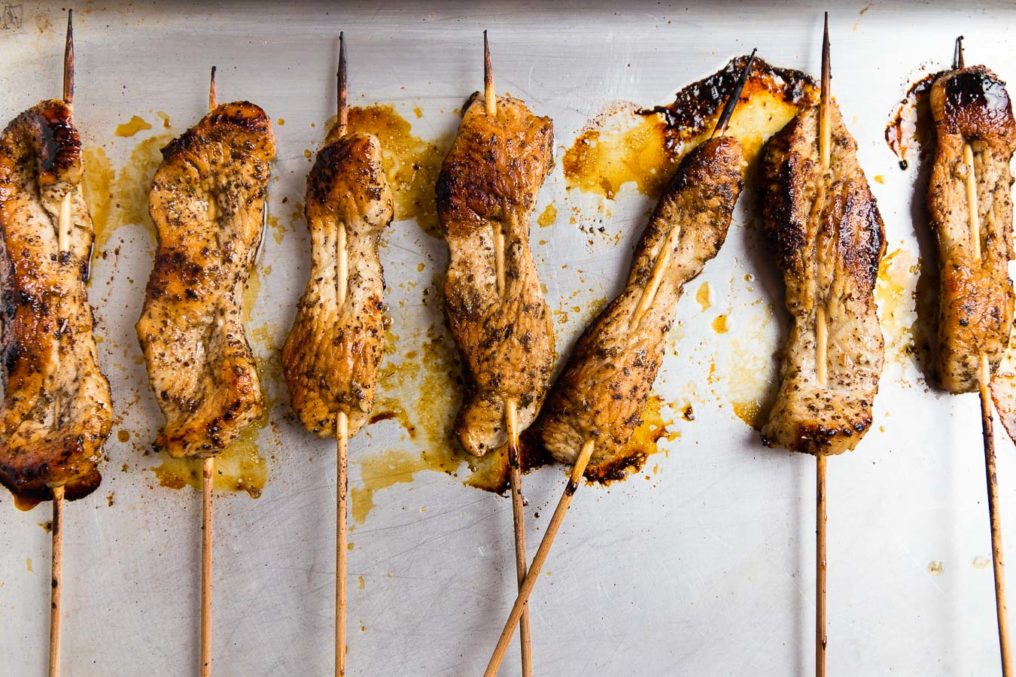 Wooden skewers through chicken pieces laying on a sliver baking tray with cooking juices