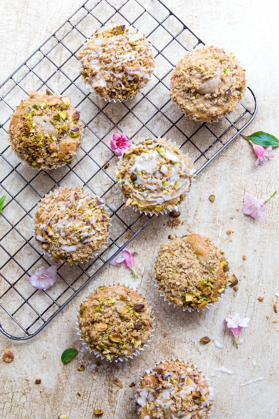 Flat lay of muffins topped with nuts on a textured background with a cooling rack and edible flowers