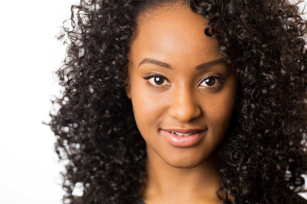 Headshot of beautiful young black female dancer with long curly hair. Talisha Thomas-Lindsay has clear catchlights in her brown eyes and the background is white