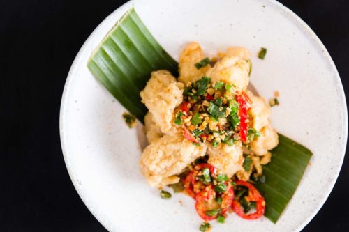 A top down photo of Thai scampi served on a white plate, green leaf with finely chopped red and green peppers with a black background