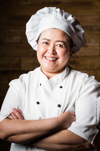 Thai female chef portrait wearing whites and a chefs hat with a wooden background