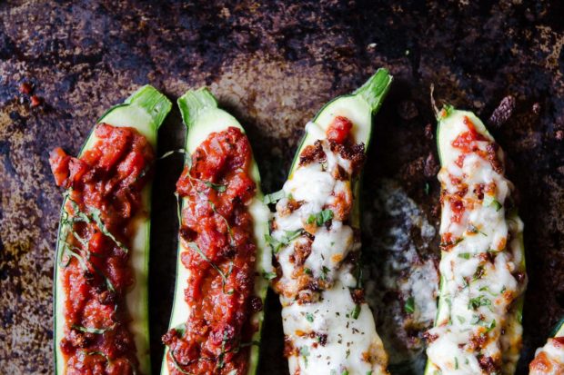Halved roasted zucchini filled with tomato sauce and cheese sit on a rustic baking sheet