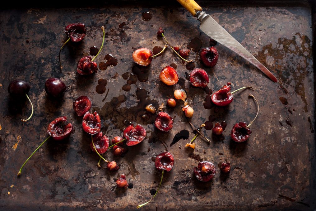 Sliced cherries on a rustic baking sheet, the knife can be seen to have cherry juice along it and juices are on the baking sheet